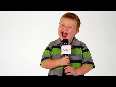 A red-haired child laughs while holding a Freshpet-branded microphone in a white studio.