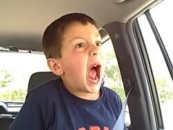 A young boy sits buckled into a car and opens his mouth wide, in another frame associated with David After Dentist.