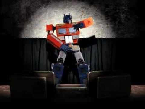 A stylized red-and-blue robot imitates a dance pose on a dark stage beneath a circular spotlight.