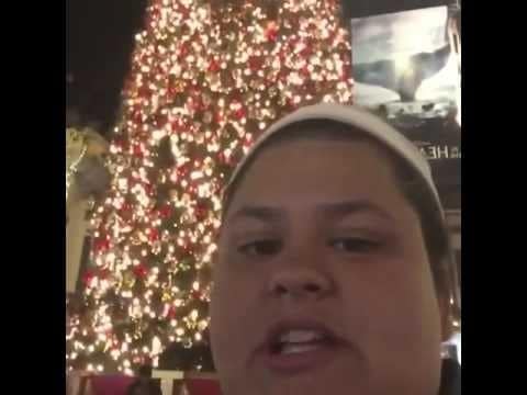 A person wearing a pale headband appears close to the camera beside a brightly lit Christmas tree in a Merry Chrysler video still.