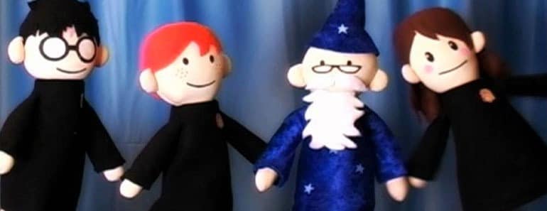 Four Potter Puppet Pals felt characters stand together against a blue curtain: a bespectacled black-haired puppet, a red-haired puppet, a blue-robed bearded puppet and a brown-haired puppet.