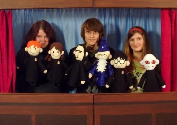Three people pose behind six Potter Puppet Pals felt puppets in front of a blue stage curtain, including red-haired, bespectacled, white-bearded and pale-faced characters.